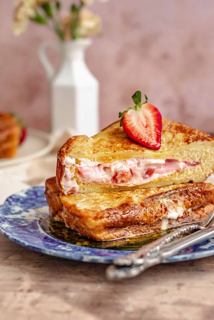 Two stuffed slices of French toast, filled with cream cheese and strawberry filling, topped with a slice of strawberry.