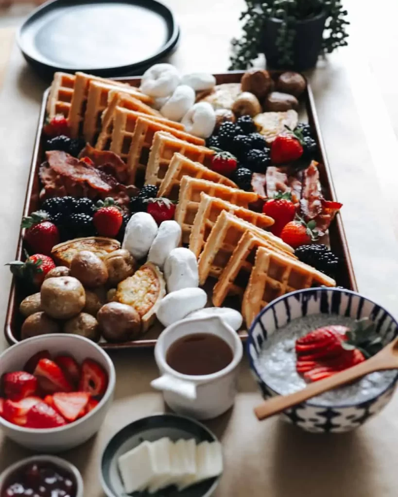 A charcuterie board with waffles, strawberries, marcshnellows, donuts, chocolate icing.