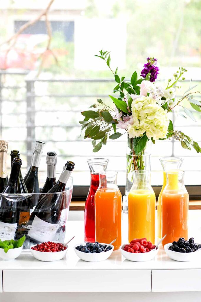 Champagne bucket filled with 4 different bottles of champagne. 4 different fruit juices and an assortment of fresh fruits in small bowls.