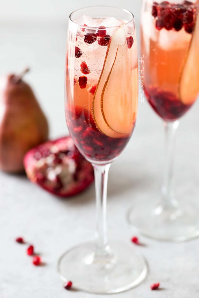A champagne flute filled with Prosecco and pomegranate seeds and pear slices.